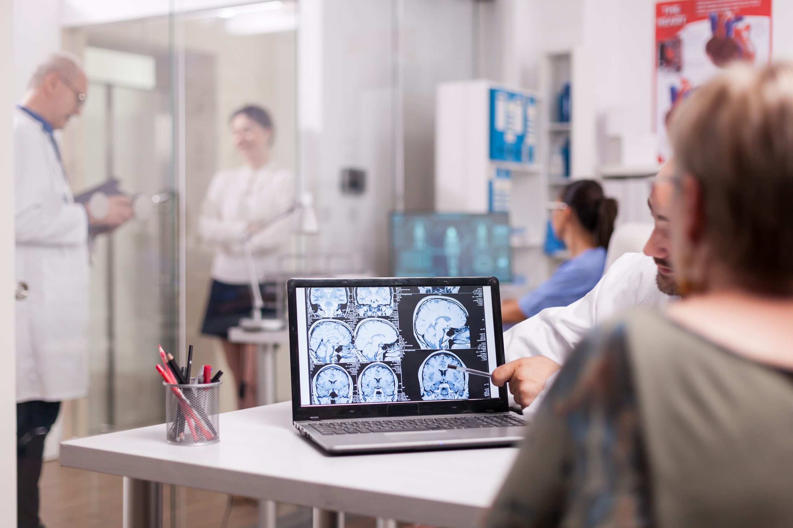 Senior woman in hospital office looking at brain ct-scan while discussing with doctor about diagnosis. Sick young woman and elderly medic with grey hair in clinic corridor.